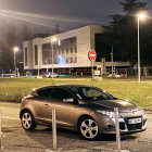 Bronze car on glittering street with modern building and "no entry" sign.