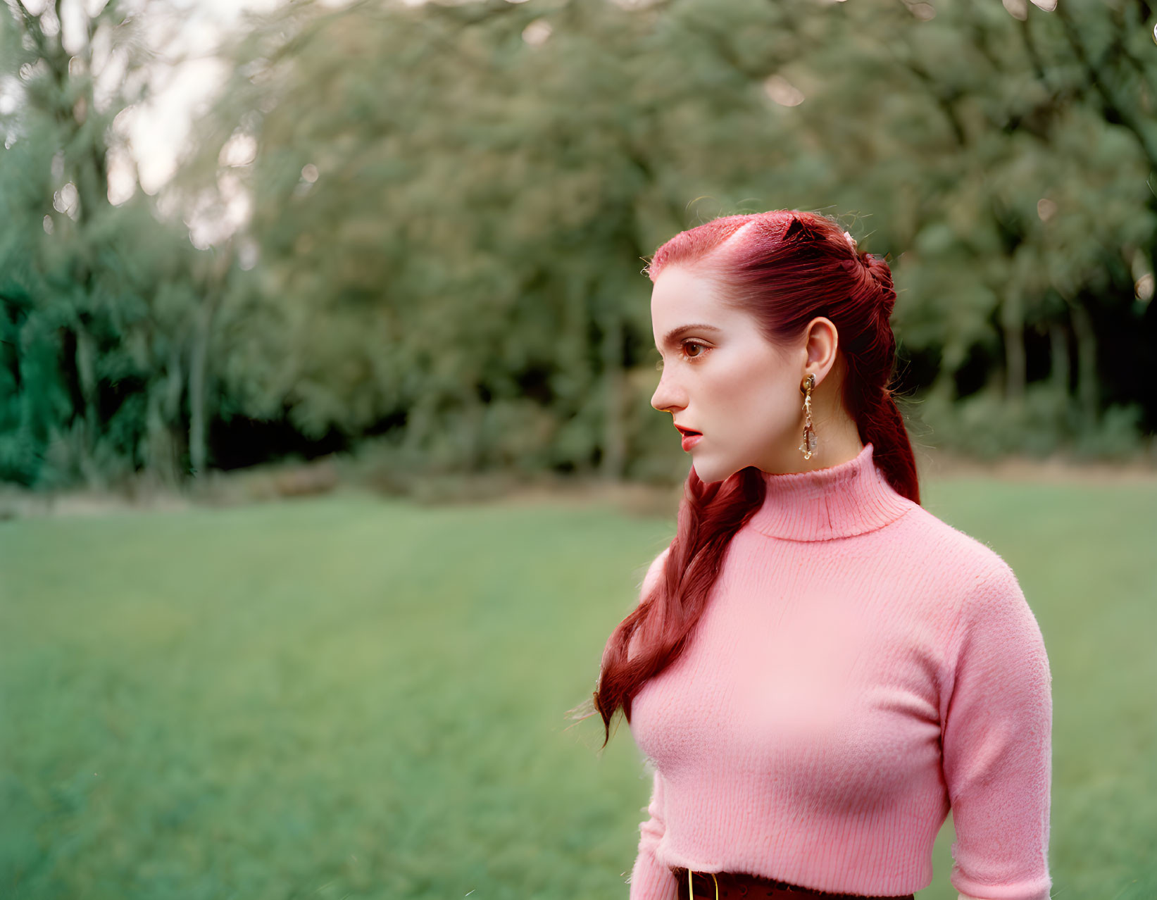 Red-haired woman in pink sweater and earrings, styled in braid, looking sideways.