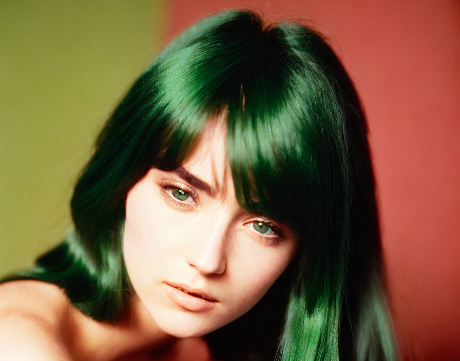 Young person with green hair and blue eyes on red-green gradient backdrop