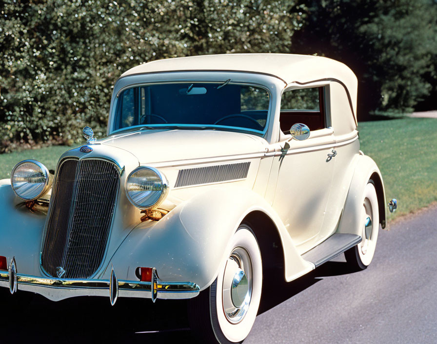 Cream Vintage Car with Distinct Grille and Chrome Accents on Greenery-Lined Road