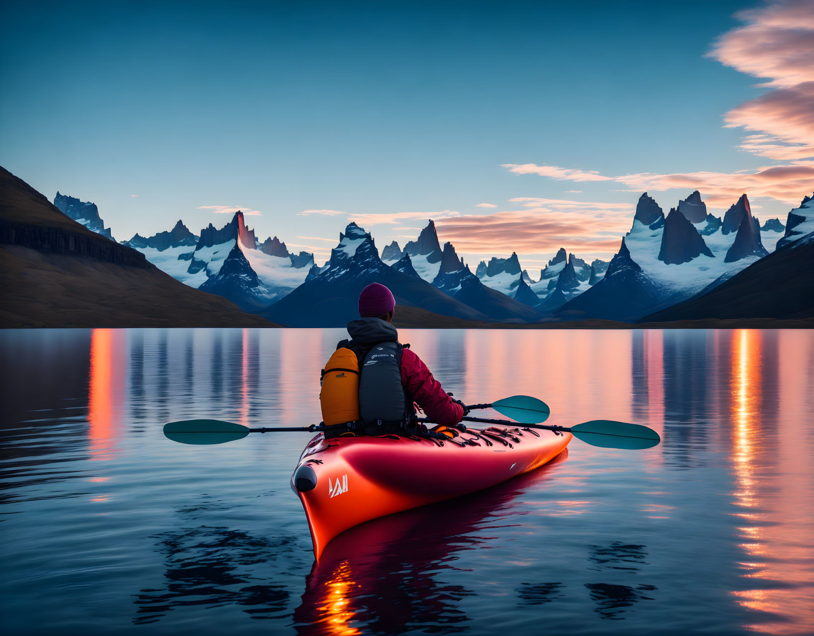 Kayaker on calm lake at sunset with sharp mountain peaks in distance