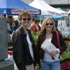 Two women in historical clothing at busy market with fruit stalls and people under large glass structure