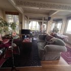 Sunlit Interior with Blue Sofa, Red Ottoman, Books, Plants, and Ocean View