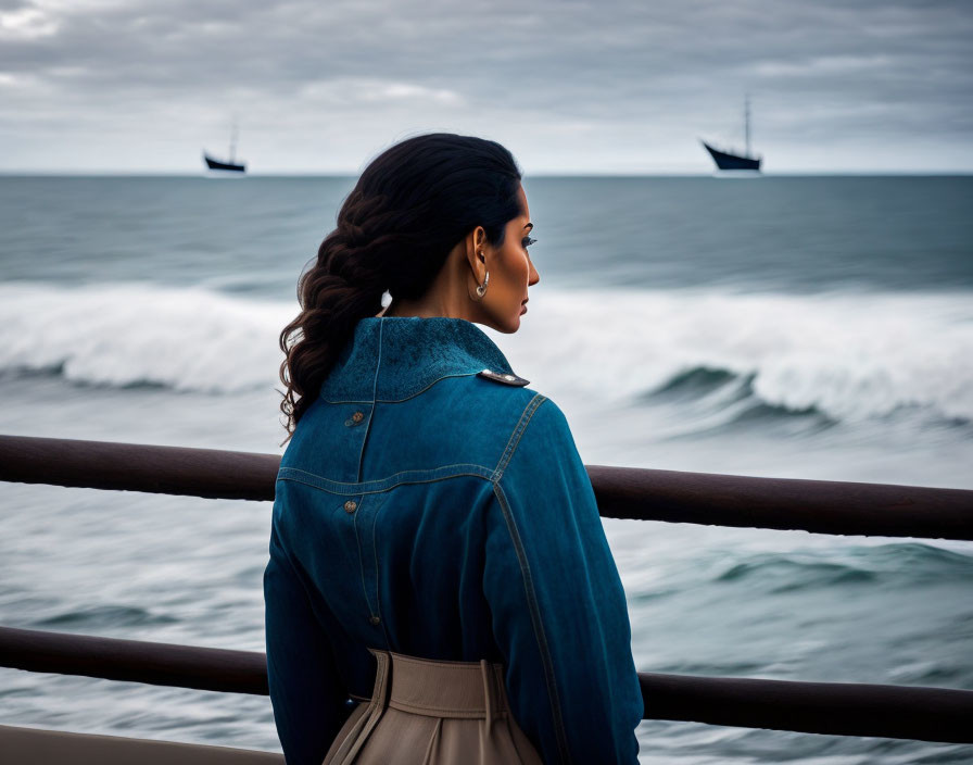 Woman in denim jacket gazes at sea with ships and waves breaking in background