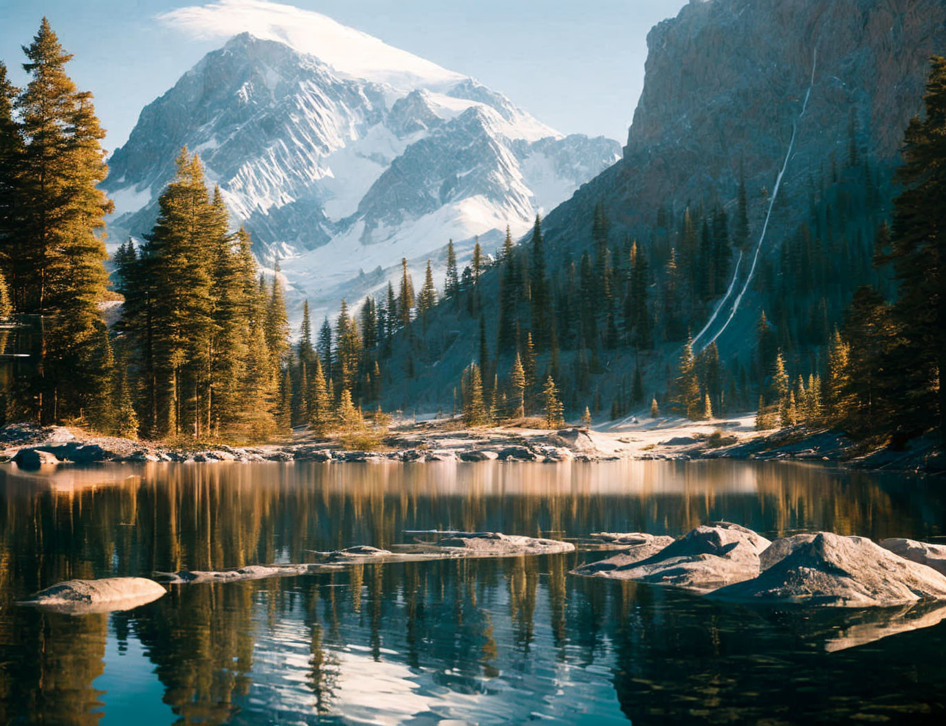 Snow-capped peaks reflected in serene lake amidst pine trees