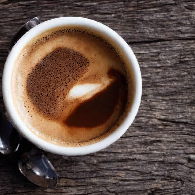 Heart-shaped latte art on wooden surface with spoon