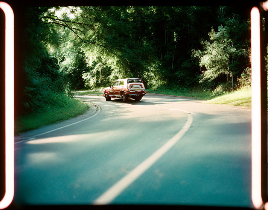 Vintage car on winding forest road with red borders.