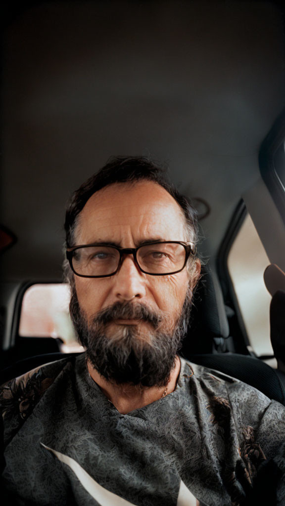 Bearded man with glasses in car passenger seat gazes thoughtfully at camera