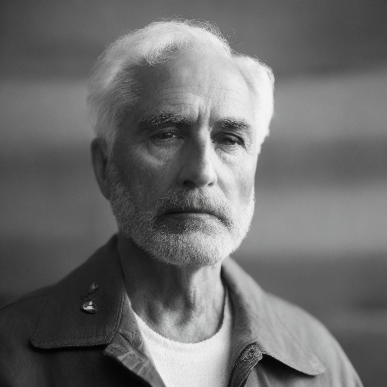 Elderly man with white beard and collared jacket gazes thoughtfully.