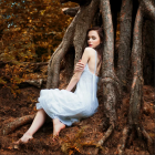 Woman in white dress beside ancient tree in autumn setting