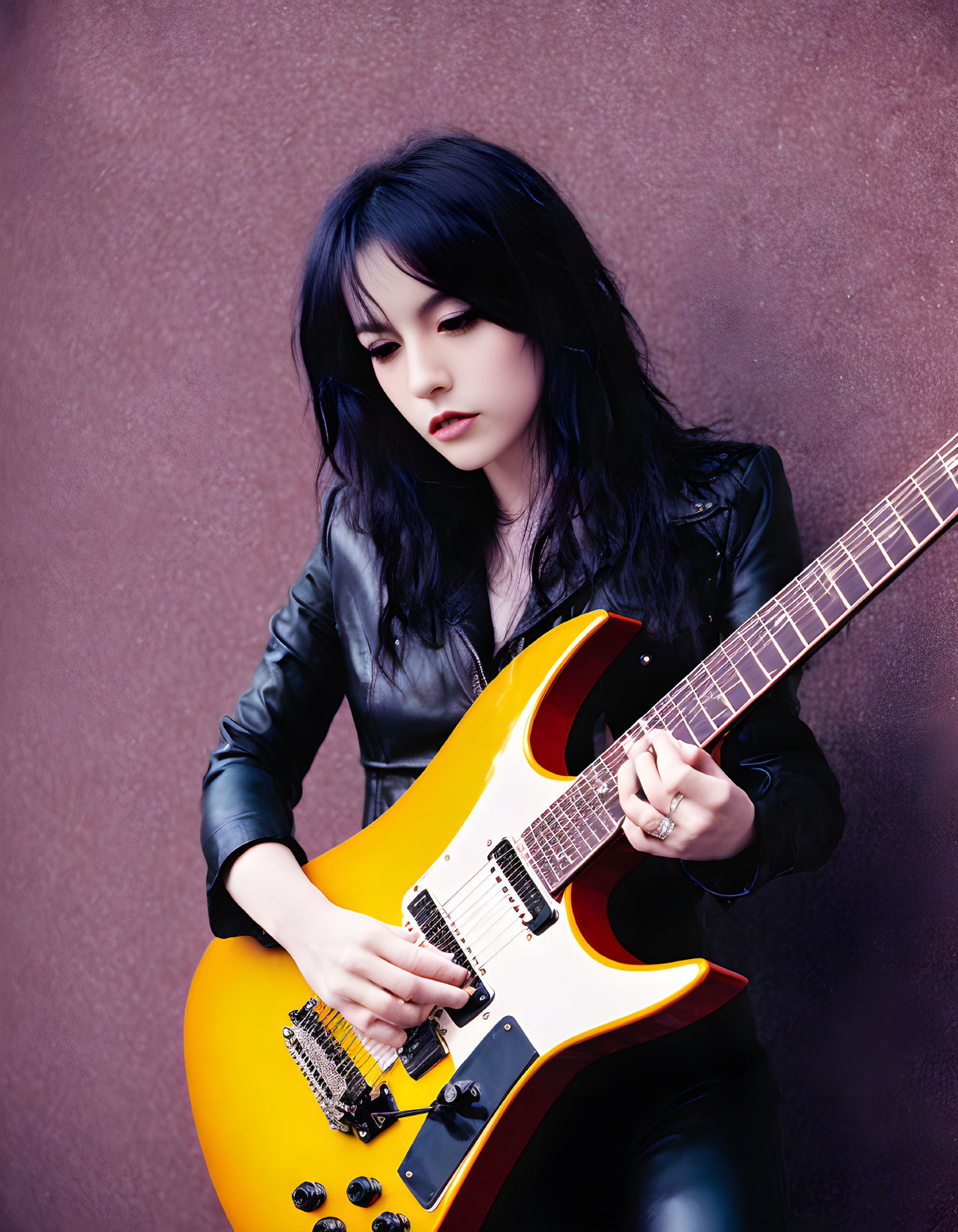Dark-haired person in black outfit plays yellow electric guitar on maroon backdrop
