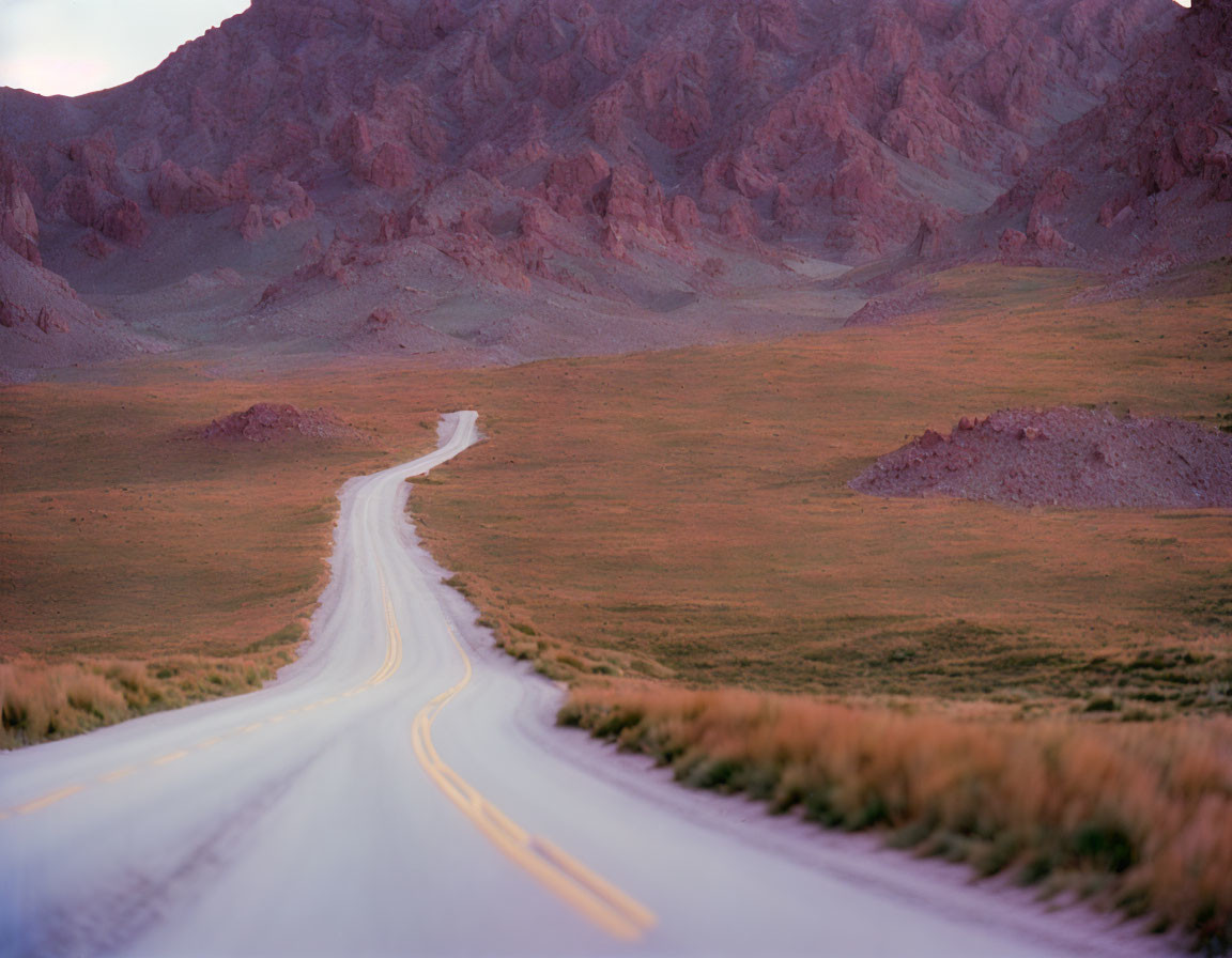 Winding Road Through Grassland with Mountain Backdrop at Dusk