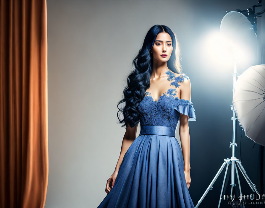 Dark-haired woman in blue off-shoulder dress poses in photo studio