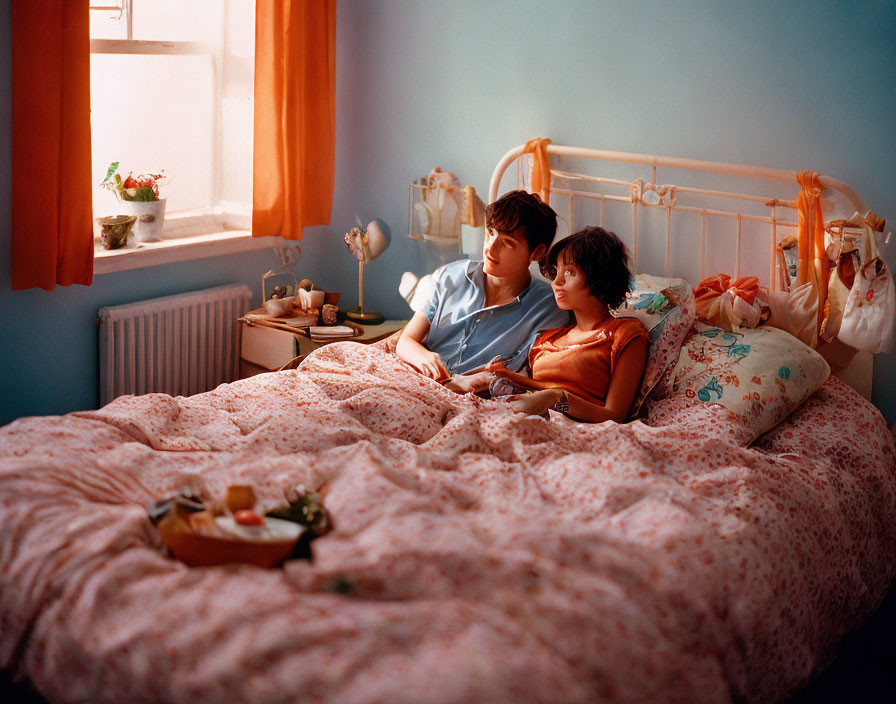 Couple Relaxing on Bed in Blue Room with Floral Comforter and Tray of Food