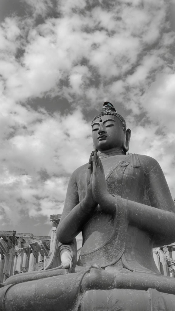 Monochrome photo: Large Buddha statue in meditative pose against dramatic sky