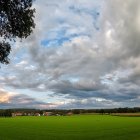 Person walking on lush grass path towards shimmering lake under vibrant sky