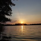 Tranquil sunset over calm lake with tree silhouettes and cloudy sky