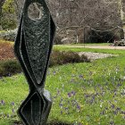 Intricate black metallic sculpture outside whimsical cottage amid lush garden