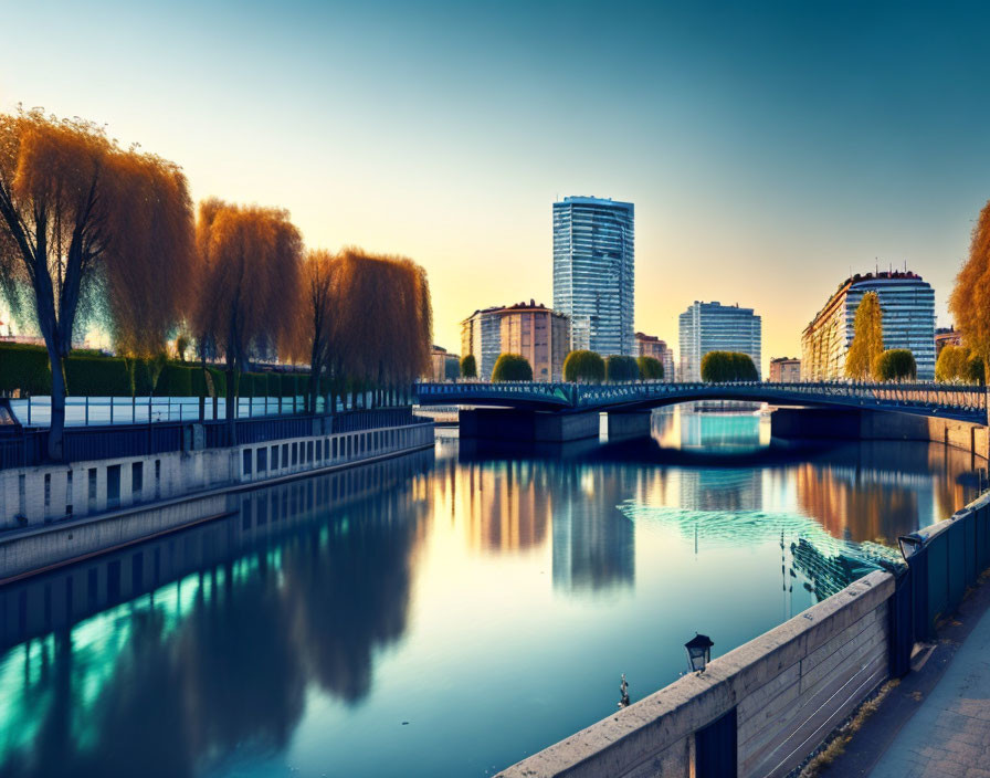 Modern urban river scene with weeping willows, clear sky, and reflections at sunrise or sunset