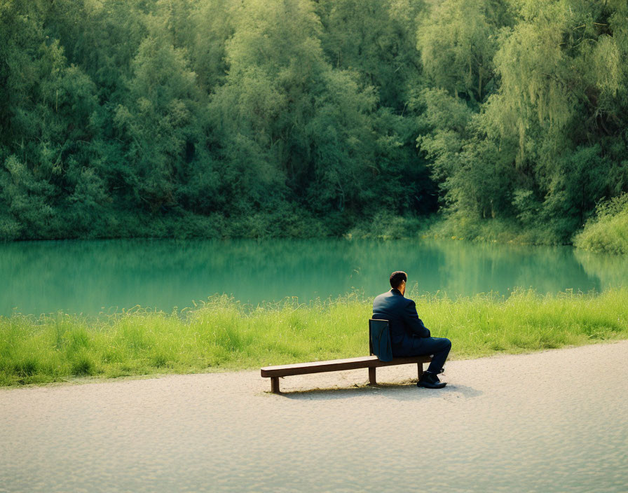 Businessperson sitting on bench by serene lake with green trees