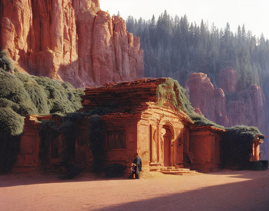 Ancient stone building with vine-covered arch against red rock cliffs.