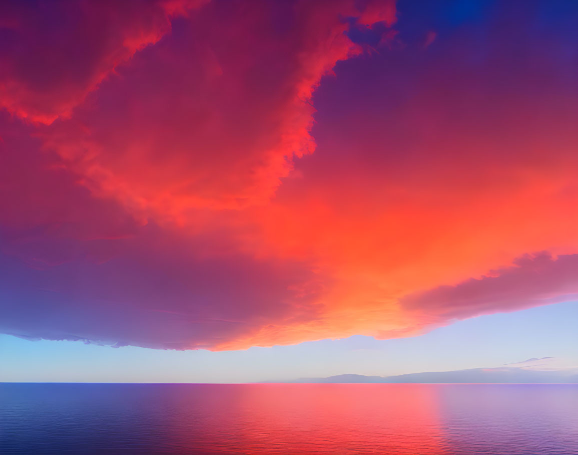 Colorful sunset skies over serene ocean with distant mountain silhouette