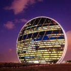 Futuristic spherical building illuminated at twilight with horizontal lights against purple sky