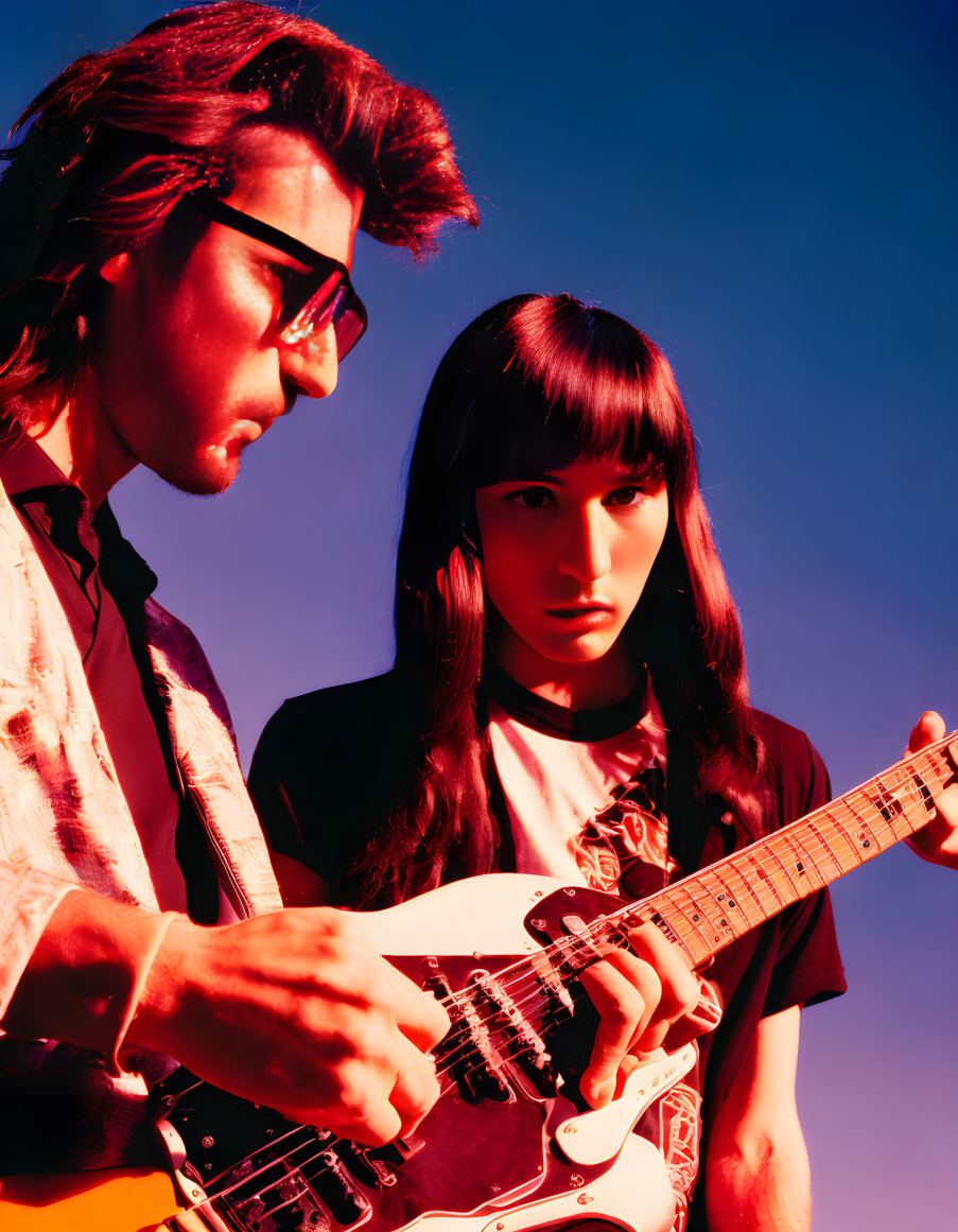 Two individuals playing guitar against purple backdrop, wearing sunglasses.