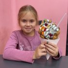 Serious young girl in pink jacket with colorful pompoms basket