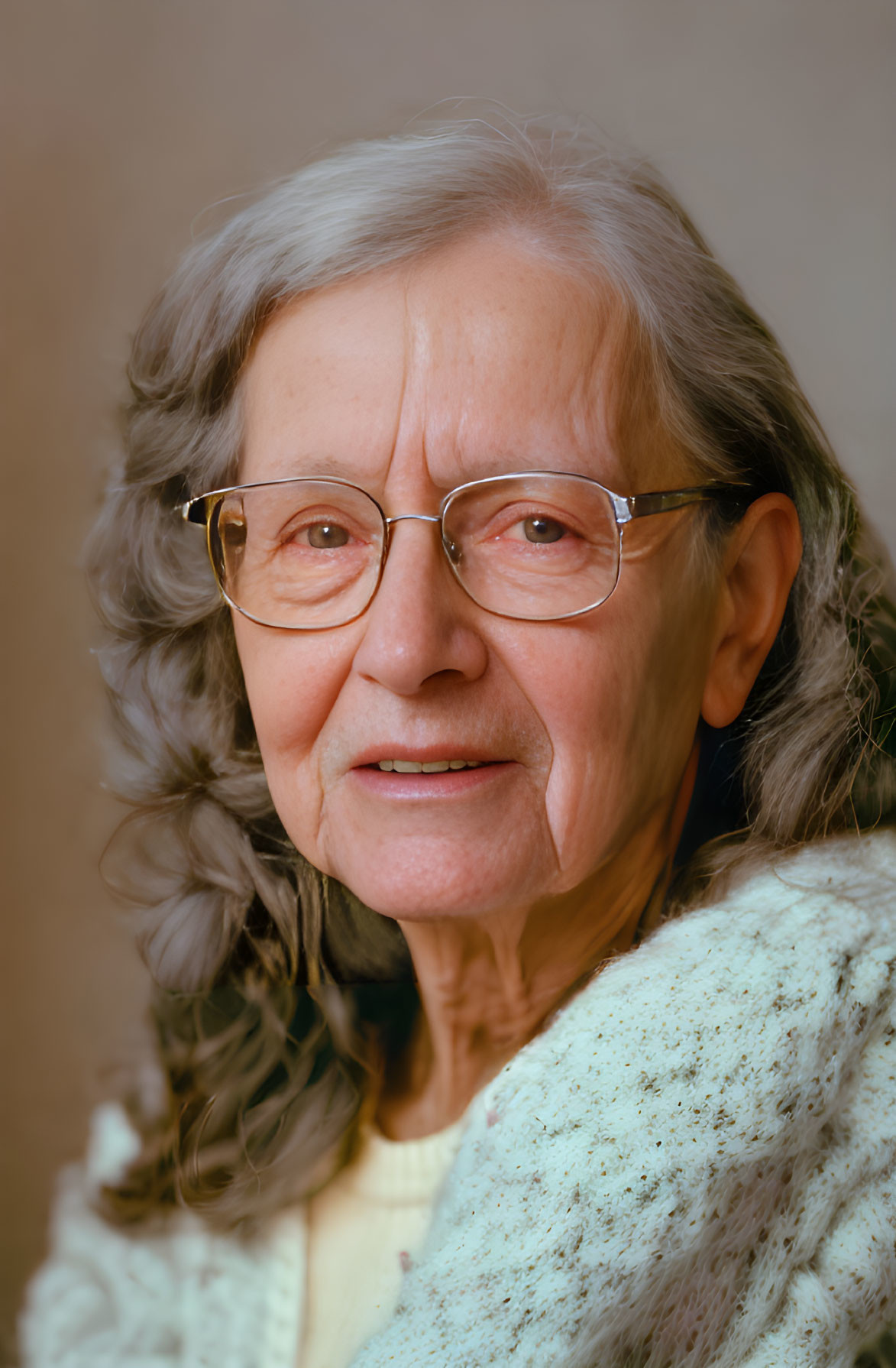 Elderly woman in glasses and cardigan smiling on beige background