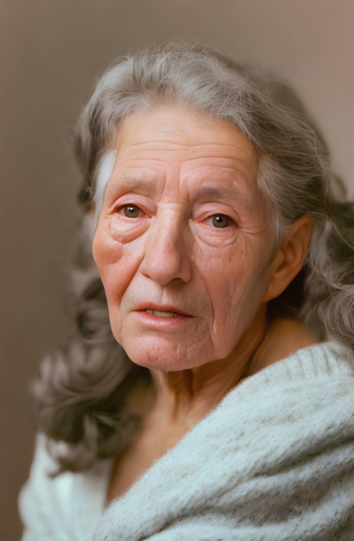 Elderly woman with grey hair and wrinkles in light blue top on neutral background