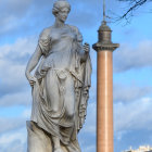 Two white sculptures of female figures in flowing robes under a blue sky with wispy clouds and a leaf