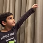 Child in superhero costume with cape and mask posing confidently against curtain backdrop