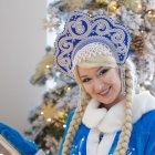 Blonde woman with berry wreath in blue cloak on snowy background