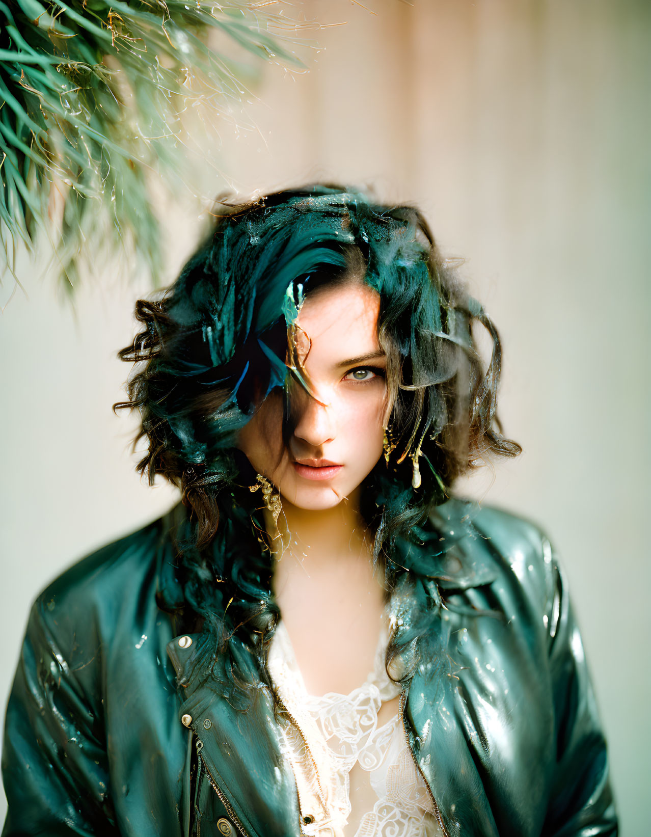 Teal-haired woman in green leather jacket with gold jewelry gazes at camera