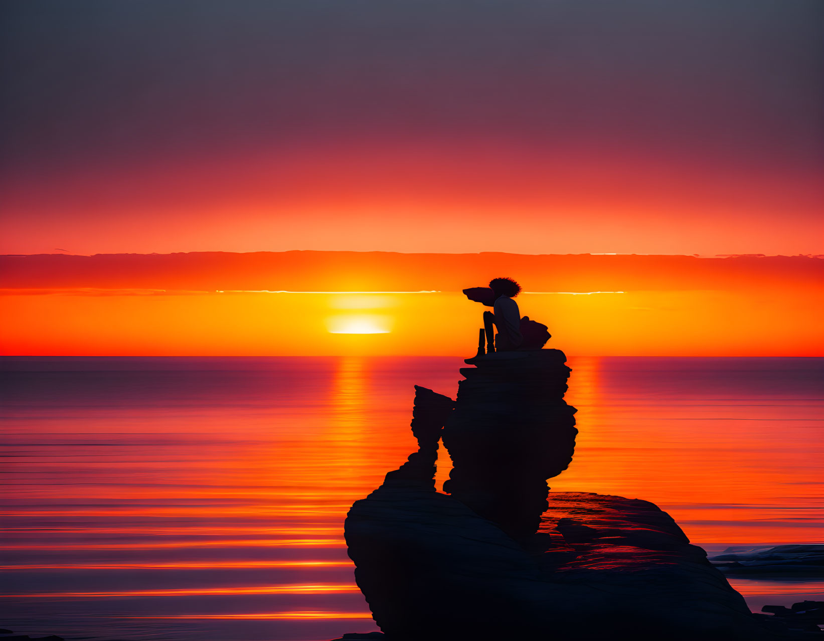 Silhouette of person on rock by sea at sunset