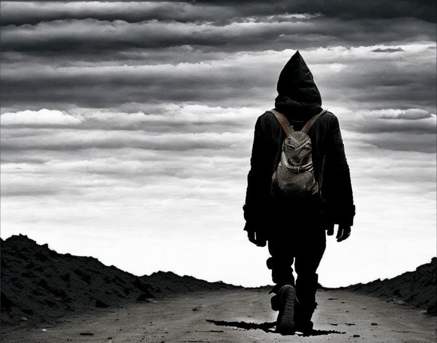 Hooded figure with backpack on desolate landscape under overcast sky