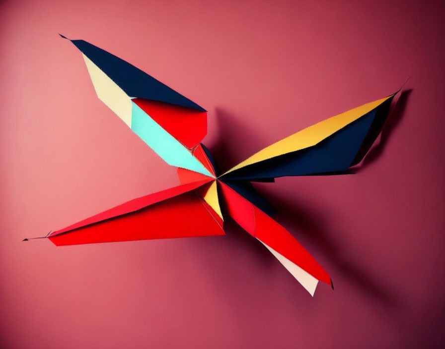 Colorful Origami Pinwheel with Red, Blue, Yellow, and White Sections on Pink Background