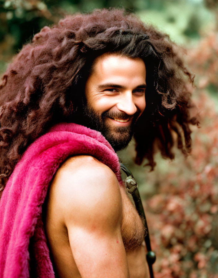 Smiling man with long curly hair and pink fur scarf in nature setting