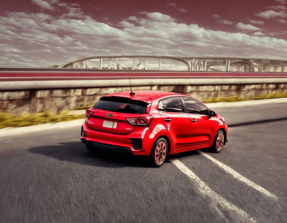 Red hatchback car speeding on road with blurred background and bridge in distance