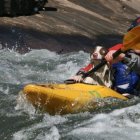 Two individuals in yellow raft navigating rough waters with paddles and helmets