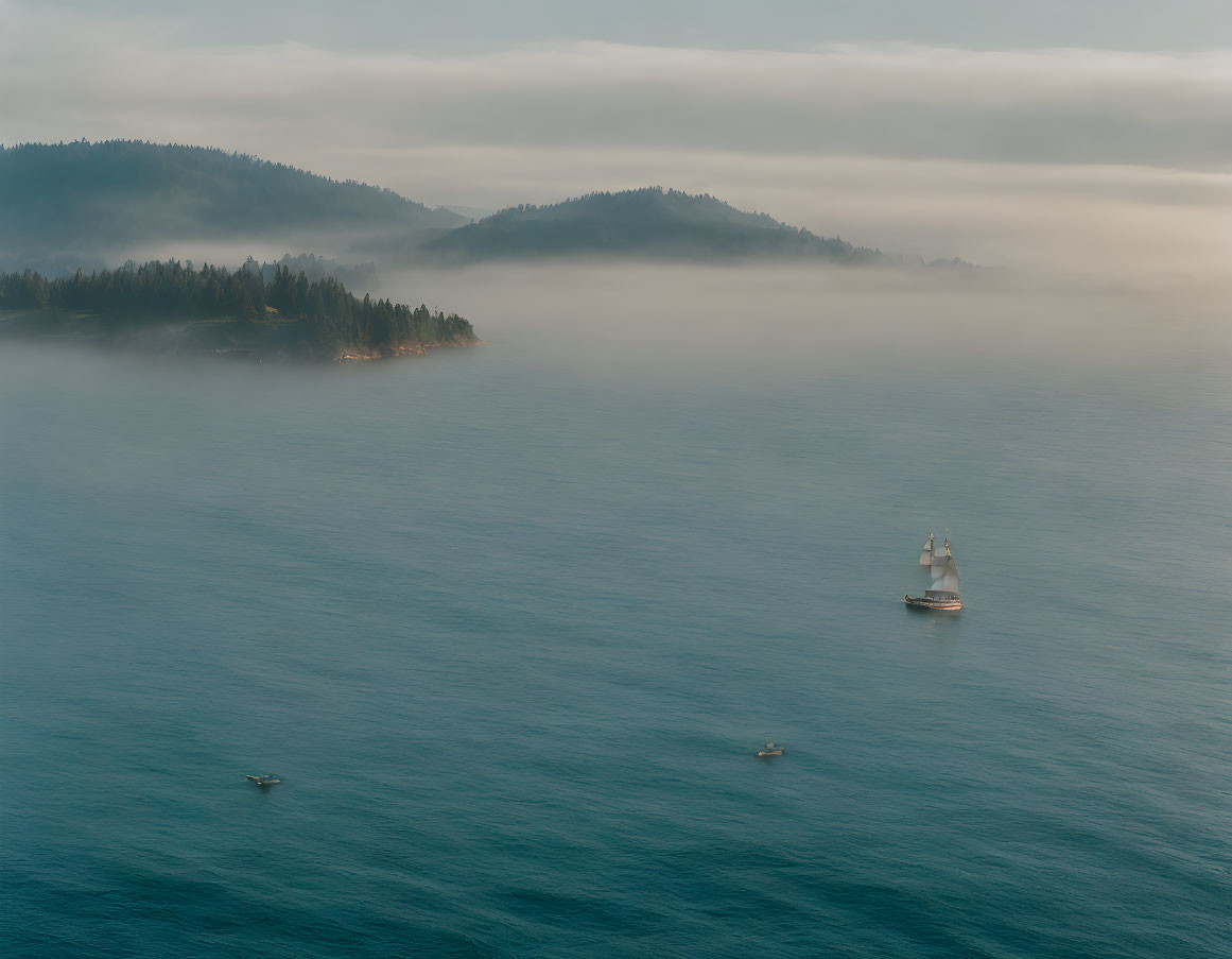 Misty sea with sailboat and forested hills