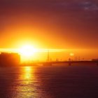Orange Sunset Silhouettes Sailboats & Cranes on Calm Sea