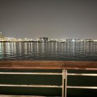 Cyclists on coastal promenade with boat and city skyline viewed from wooden pier