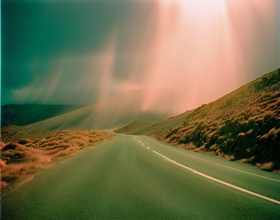 Empty Road in Hilly Landscape Under Dramatic Sky with Sunbeams