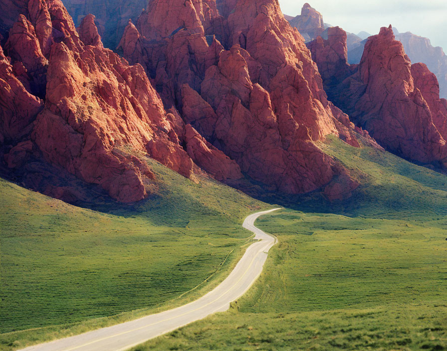 Scenic winding road in lush valley with red rocky mountains