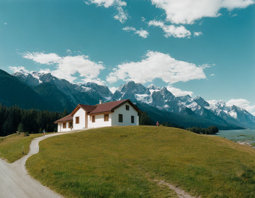 Secluded house on grassy hillock with snow-capped mountains