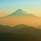 Snow-capped volcanic mountain in misty landscape under golden sky