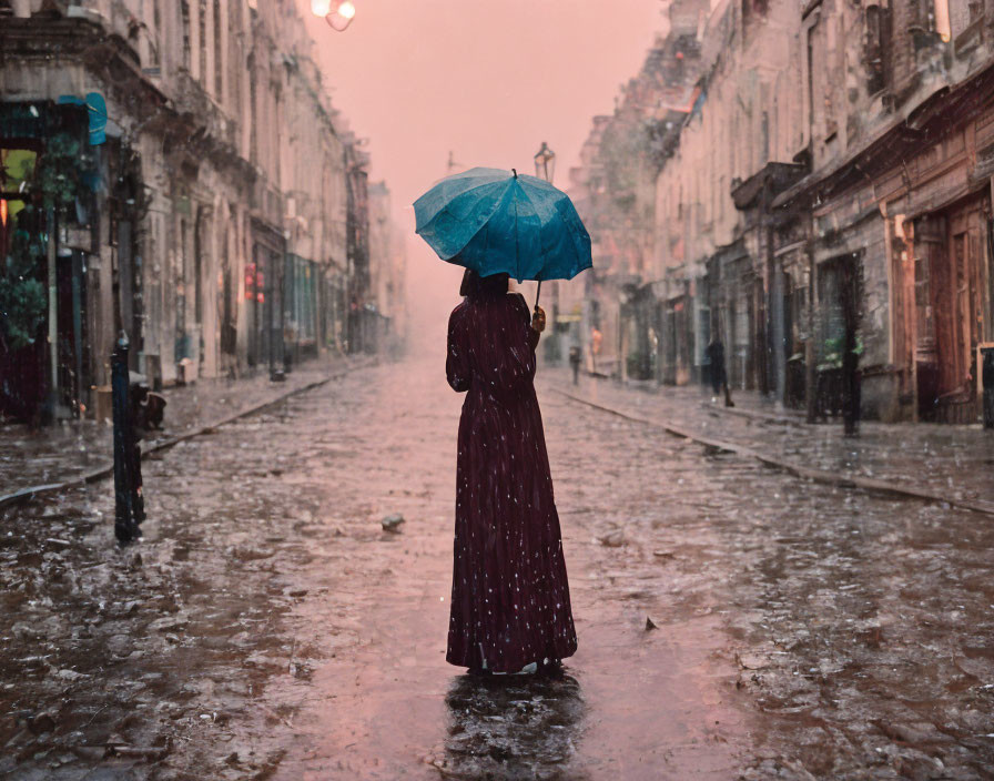 Person in Long Coat with Blue Umbrella in Rainy Urban Scene