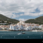 Coastal town with white buildings, church, and fish tail sculpture under cloudy sky.